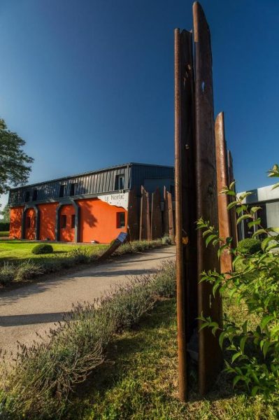 Esculturas de acero oxidado en el jardín exterior del Hotel Le Noirlac con fachada naranja al fondo
