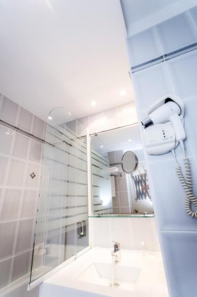 Baño moderno con ducha de cristal, lavabo y secador de pared en el Hotel Le Noirlac