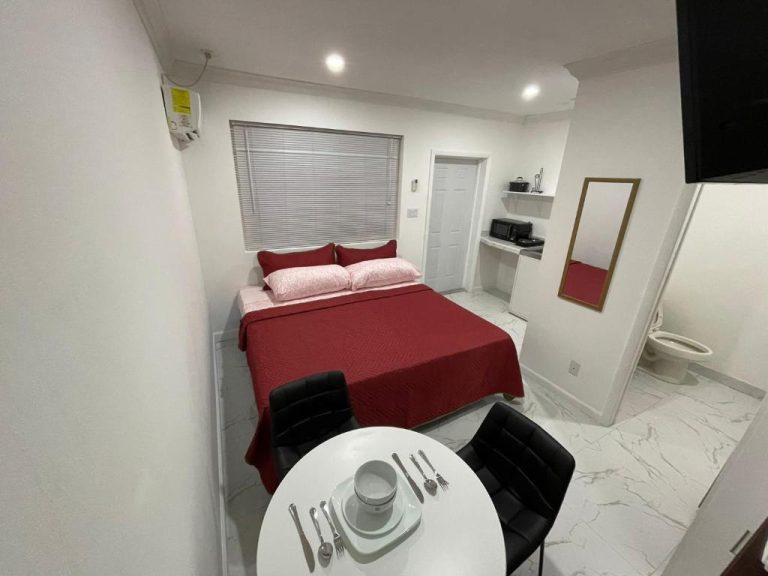 Habitación estudio con cama matrimonial roja, mesa de comedor y espejo en Sandelwood Studios