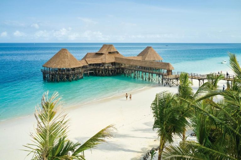Restaurante sobre el agua con techos de palapa y playa de arena blanca en Hotel Riu Jambo Zanzíbar