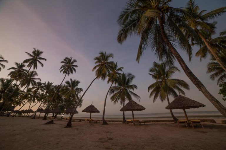 Playa con palmeras tropicales y sombrillas de paja al atardecer en Antonio Beach Hotel & Spa de África Oriental