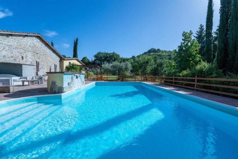 Piscina exterior de aguas cristalinas con vistas al jardín y colinas del Agriturismo I Pietrini