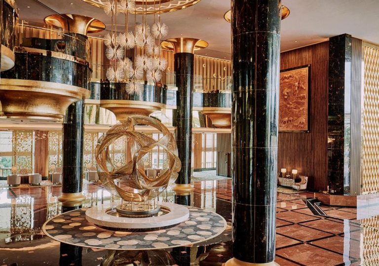 Lujoso lobby del Sunway Resort Hotel con escultura dorada, columnas de mármol y lámparas exclusivas