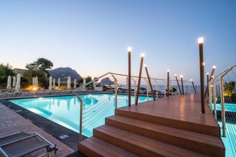 Piscina exterior iluminada al atardecer con vistas al mar en el Hotel Domina Zagarella Sicily