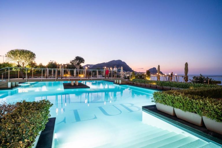 Piscina exterior iluminada al atardecer con vistas al mar en Domina Zagarella Sicily