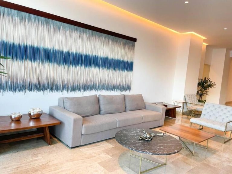 Sala de estar moderna con sofá gris y arte textil azul en hotel Ipana by Andiani Travel