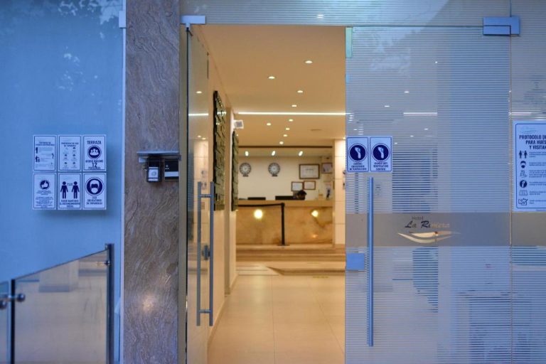 Entrada principal con puertas de cristal y recepción del Hotel La Riviera con protocolos de seguridad
