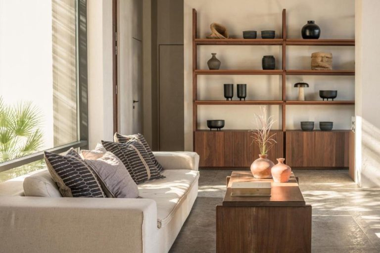 Salón elegante con sofá blanco, mesa de madera y estantería con cerámica artesanal en Lindos Aqua Terra