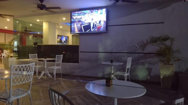 Terraza bar del Plaza Coral Hotel con mesas blancas, sillas y televisión en la pared