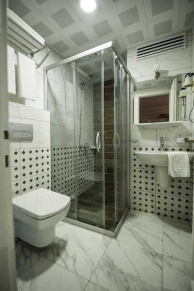 Baño moderno con ducha de cristal y suelo de mármol blanco en Narcis Apart Hotel