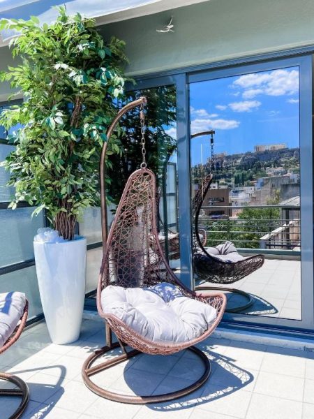 Terraza con sillas colgantes de mimbre y vistas a la Acrópolis de Atenas en Royalty Suites Psyrri