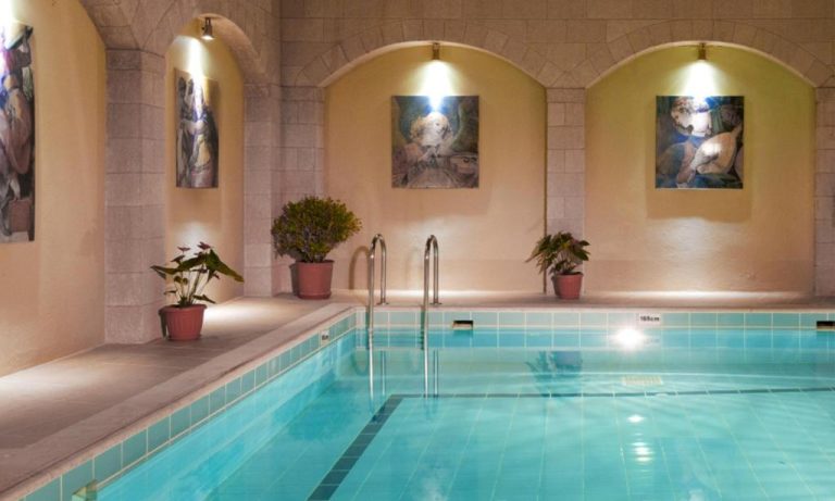 Piscina interior climatizada con arcos de piedra y obras de arte del Alexandra Hotel & Apartments