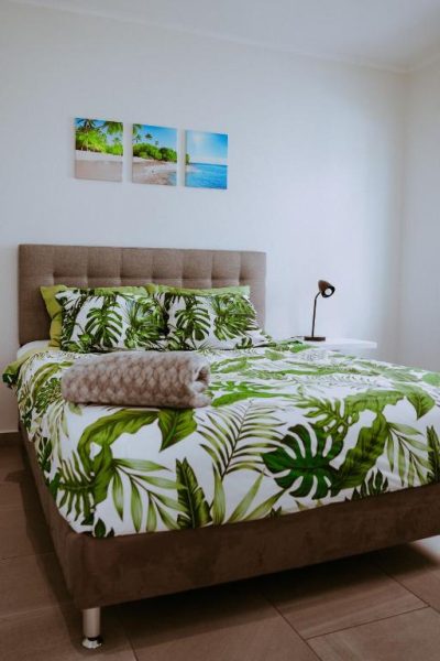 Habitación doble con decoración tropical y ropa de cama de hojas verdes en The Palm Leaf Apartments