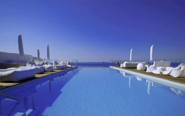 Piscina infinita con tumbonas blancas y vistas al mar en el hotel The Sindbad