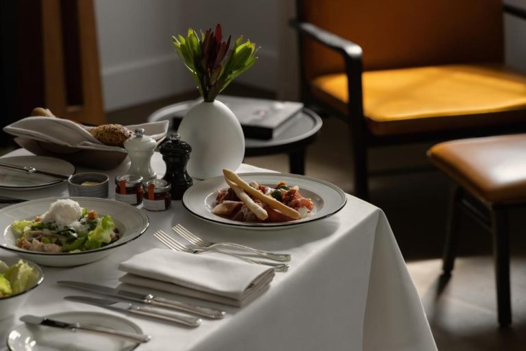 Mesa elegante con platos gourmet y decoración floral en el restaurante del Capella Sydney
