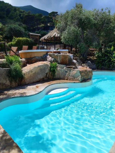 Piscina exterior de forma orgánica con rocas naturales y jacuzzi en Marettimo Residence