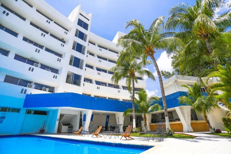 Piscina exterior con palmeras y tumbonas del Hotel Caribe Internacional Cancún rodeada de edificio blanco y azul