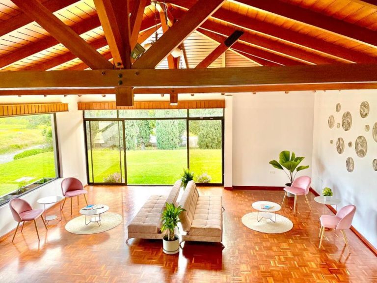 Sala de estar con sofá blanco, sillas rosas y techo de madera en Quito Airport Suites Hotel