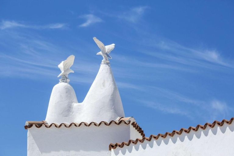 Chimeneas decorativas blancas con esculturas de águilas en la fachada del Sulià House Porto Rotondo Hilton
