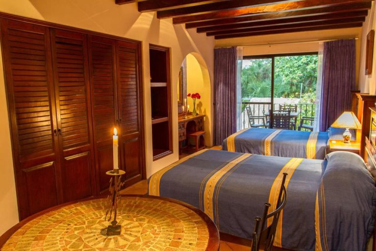 Habitación doble con camas azules y doradas, decoración colonial y balcón con jardín en Hotel Lunata 5th Avenue