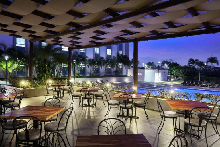 Terraza exterior con mesas y sillas del DoubleTree by Hilton Managua con vista a la piscina iluminada de noche
