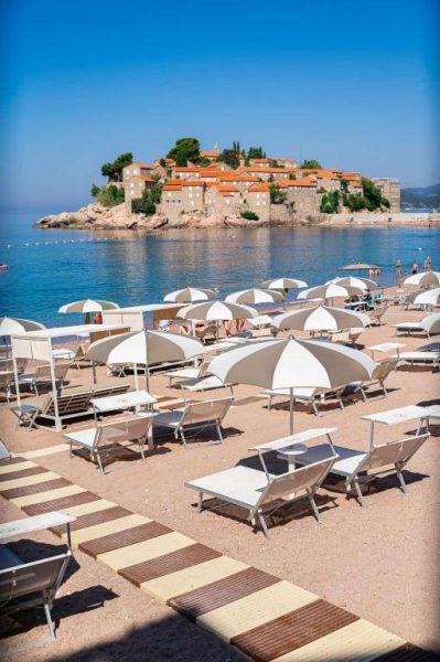 Playa con tumbonas y sombrillas blancas del Hotel California by Aycon con vistas a la isla de Sveti Stefan
