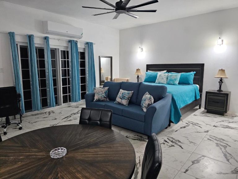 Amplia habitación suite con cama king, sofá azul y suelos de mármol en Roots Cafe Negril Rooms