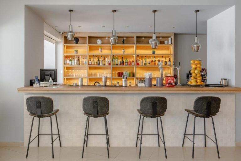 Bar del Areti Hotel con taburetes, estantería iluminada y variedad de licores y bebidas