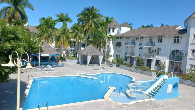 Piscina exterior con tobogán acuático y bar de playa en Beach One Bedroom 2, rodeada de palmeras