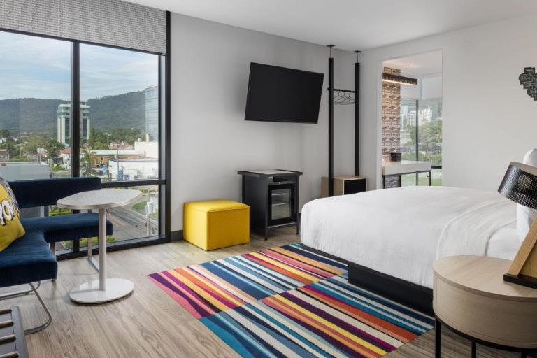 Habitación king moderna con alfombra colorida y vista a la ciudad en Aloft Marriott San Pedro Sula