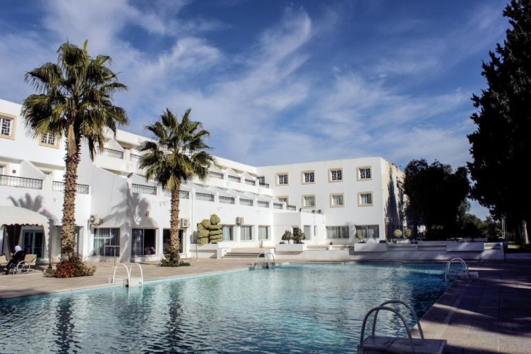 Piscina exterior con palmeras y fachada blanca del Hotel Continental en día soleado