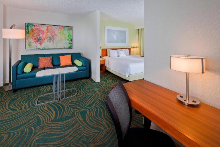Suite con salón, sofá azul, escritorio y dormitorio en SpringHill Suites Orlando Lake Buena Vista