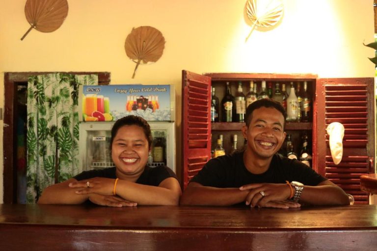 Personal del bar del Sambor Village Hotel posando sonrientes tras la barra con botellas al fondo