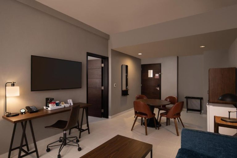 Sala de estar con escritorio, mesa de comedor y TV en Four Points by Sheraton Puntacana