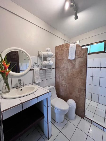 Baño completo con ducha de azulejo, lavabo y toallas en Hotel Villas de la Colina