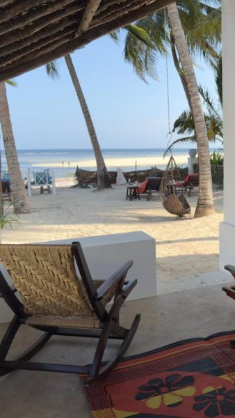 Terraza con sillas de madera y vista a la playa de palmeras en Sawa Sawa Beach House