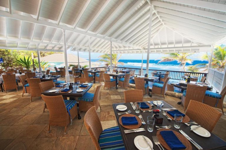 Restaurante terraza del The Atlantis Historic Inn con mesas y sillas de mimbre y vistas al mar Caribe