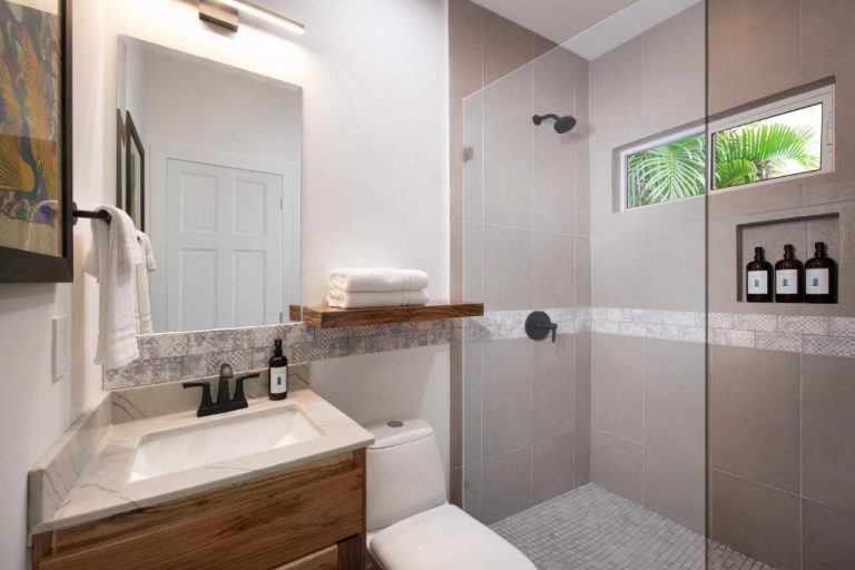 Baño moderno con ducha de azulejos y ventana con vistas al jardín tropical en Hotel Puerta Azul