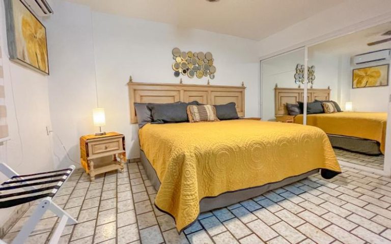 Habitación con cama doble y colcha amarilla en Playa Bonita Beso del Sol 101 con espejo y aire acondicionado