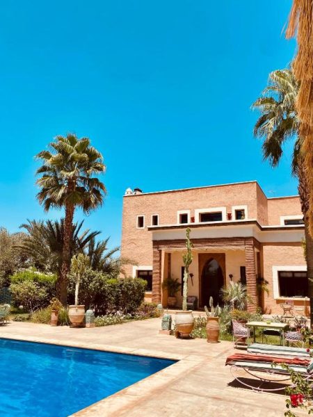 Piscina exterior con villa de estilo marroquí y palmeras en La Villa Des Golfs & PinkCactus Marrakech