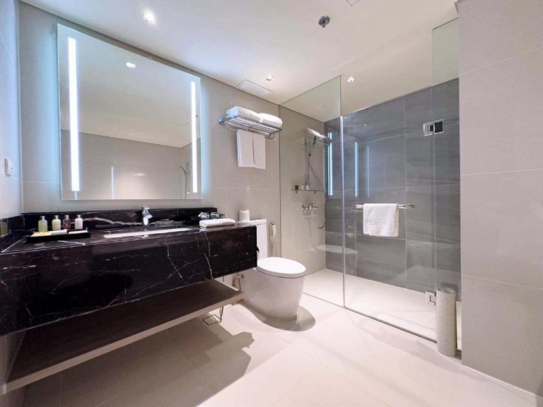 Baño moderno con ducha de cristal y encimera de mármol negro en el hotel Seda Nuvali Laguna