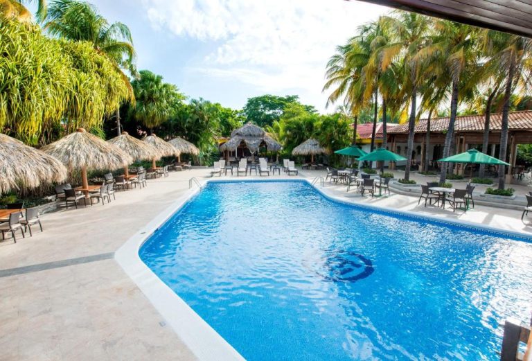 Piscina exterior rodeada de palmeras y palапас en el Hotel Globales Camino Real Managua