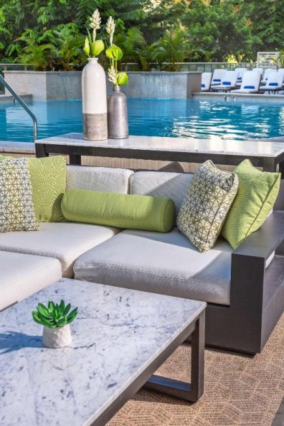 Terraza con sofás y cojines verdes junto a la piscina exterior del Hilton Garden Inn Waikiki Beach