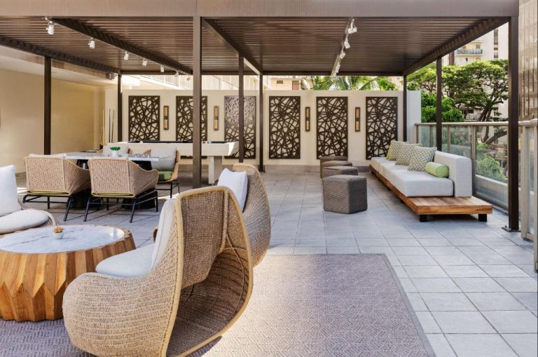 Terraza lounge con sillones de mimbre y sofás blancos en el Hilton Garden Inn Waikiki Beach