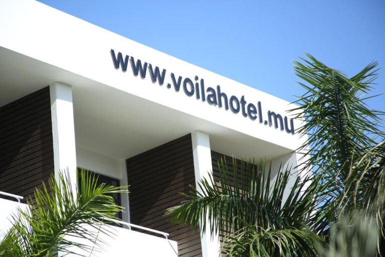Fachada exterior moderna del Hotel Voila Bagatelle con palmeras tropicales bajo cielo azul