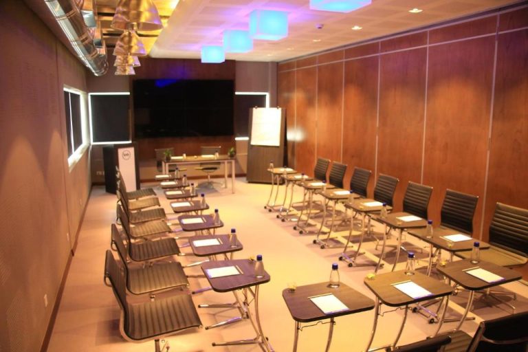 Sala de reuniones y conferencias del Voila Bagatelle con mesas individuales, pantalla y pizarra