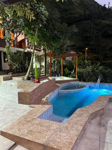 Piscina exterior iluminada con jacuzzi y cascada del Spa Hotel Etelvina rodeada de montañas