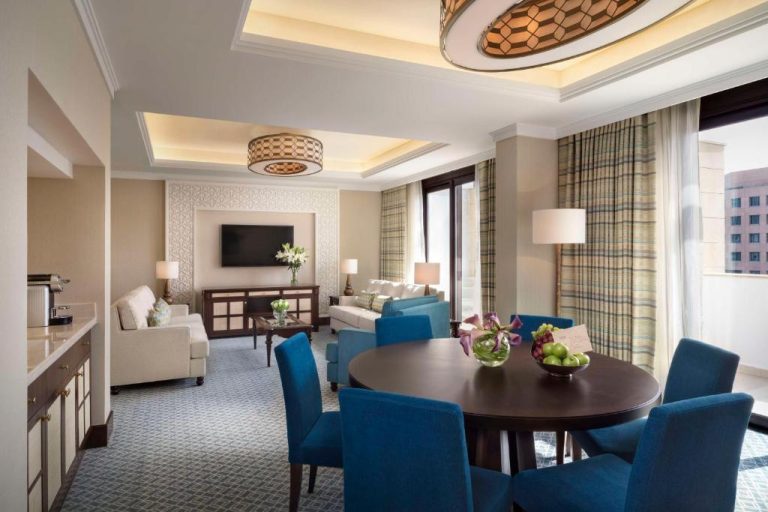 Suite con salón y comedor elegante de sillas azules en Al Najada Doha Hotel by Tivoli