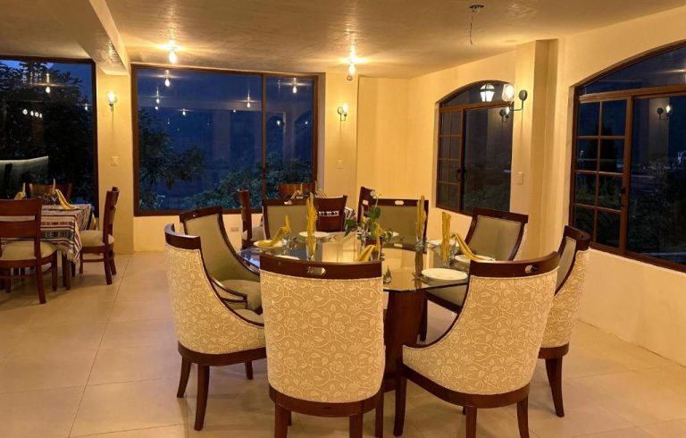 Elegante comedor del Spa Hotel Etelvina con mesa redonda de cristal y sillas tapizadas con vistas nocturnas al jardín