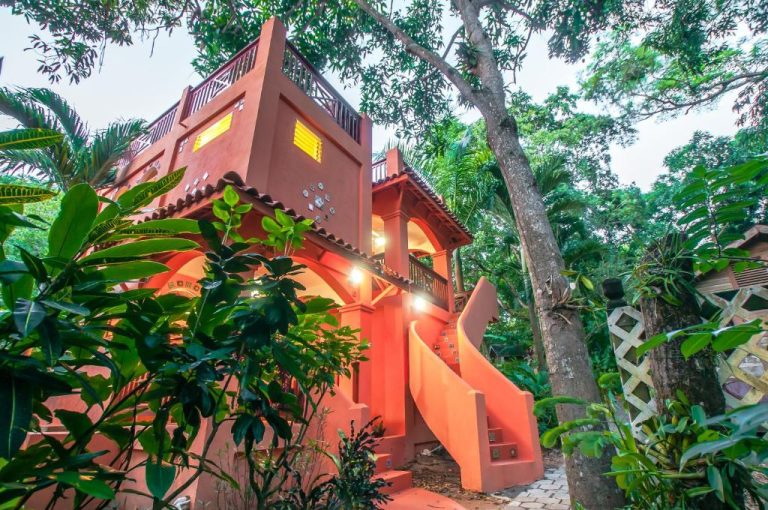 Fachada colonial roja del Hotel Chillies and Native Sons Diving rodeada de vegetación tropical exuberante